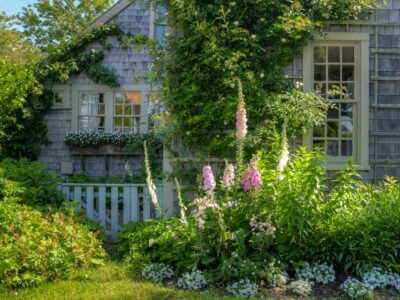 Ceder shingled house with flowerin in front.