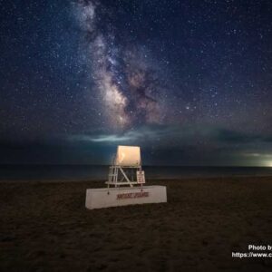 Life Guard chair on a beach under a vibrant night sky.