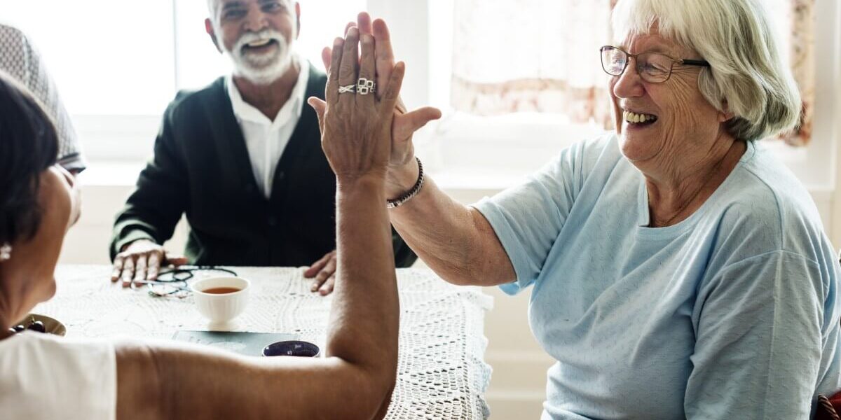 Two senior women giving a high five while sitting at a table.