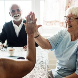 Two senior women giving a high five while sitting at a table.